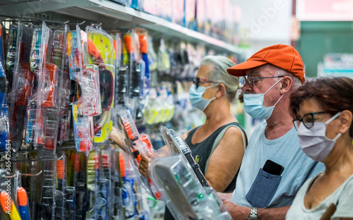 Three senior people shopping together in sea accessories department choosing a scuba mask, wearing medical mask due to coronavirus