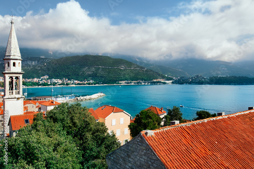 Obraz na płótnie Church tower and red roofs of ancient town Budva and Adriatic sea coast. Medieval architecture.White clouds blue sky and aqua green sea water background w salonie