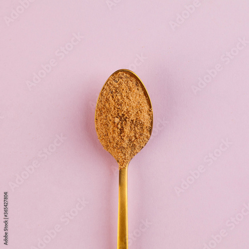 Coconut sugar in a Golden spoon on a pink background. Minimalism. The concept of healthy eating. Copy space.