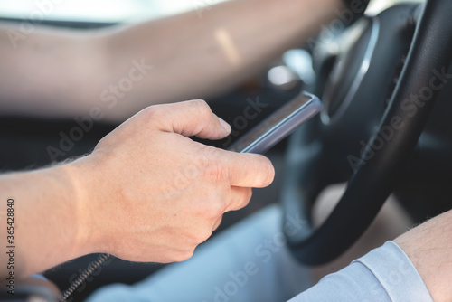 Driver with mobile phone is sitting by a steering wheel of car.