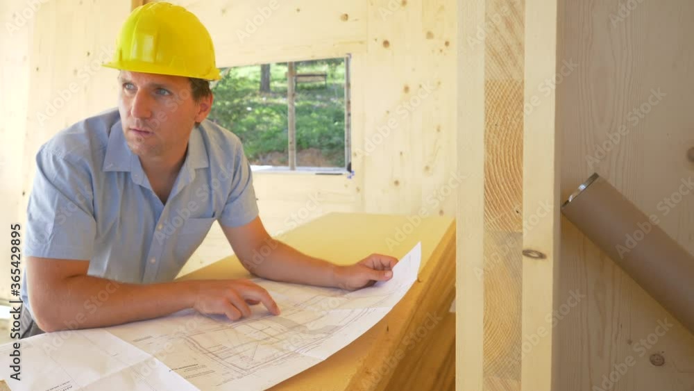 SLOW MOTION, CLOSE UP, PORTRAIT: Male architect wearing a yellow hard hat smiles after seeing construction is going according to plan. Construction site manager smiles after analysing the blueprints. SLOW MOTION, CLOSE UP, PORTRAIT: Male architect wearing a yellow hard hat smiles after seeing construction is going according to plan. Construction site manager smiles after analysing the blueprints.