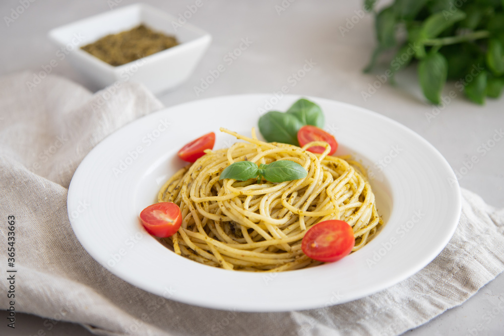 Top view on a plate with traditional Italian pesto pasta garnished with slices of cherry tomatoes and basil leaves