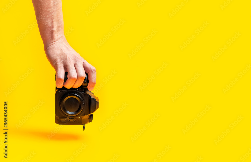 Modern SLR and mirrorless camera in male hands on yellow background flat lay copy space. Digital photography, body without lens, photographer's technique, digital camera, professional photo camera