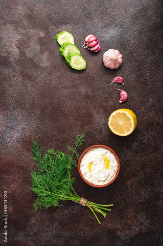 Traditional greek tzatziki sauce with ingredients on dark rustic background. Greek yogurt with cucumber, dill, garlic and lemon. Top view, copy space, flat lay.
