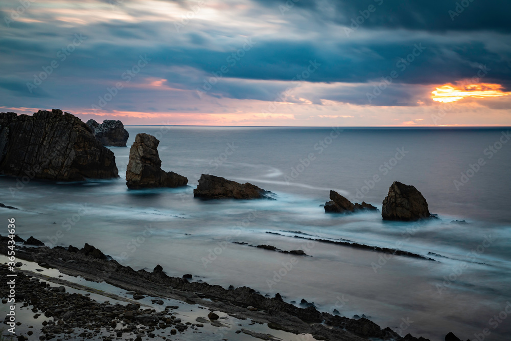 Long exposure over calm sea with rocks during a cloudy sunset