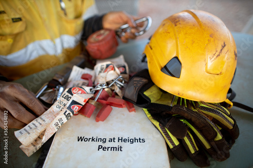 Safety workplace working at height permit book helmet personal locks place on the table with defocused inspector inspecting an inertia reel shock absorbing fall protection device prior used background photo