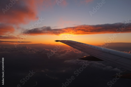 Spectacular sunset from inside an airplane over clouds a valley and a river with the left plane wing visible and the horizon mid frame.