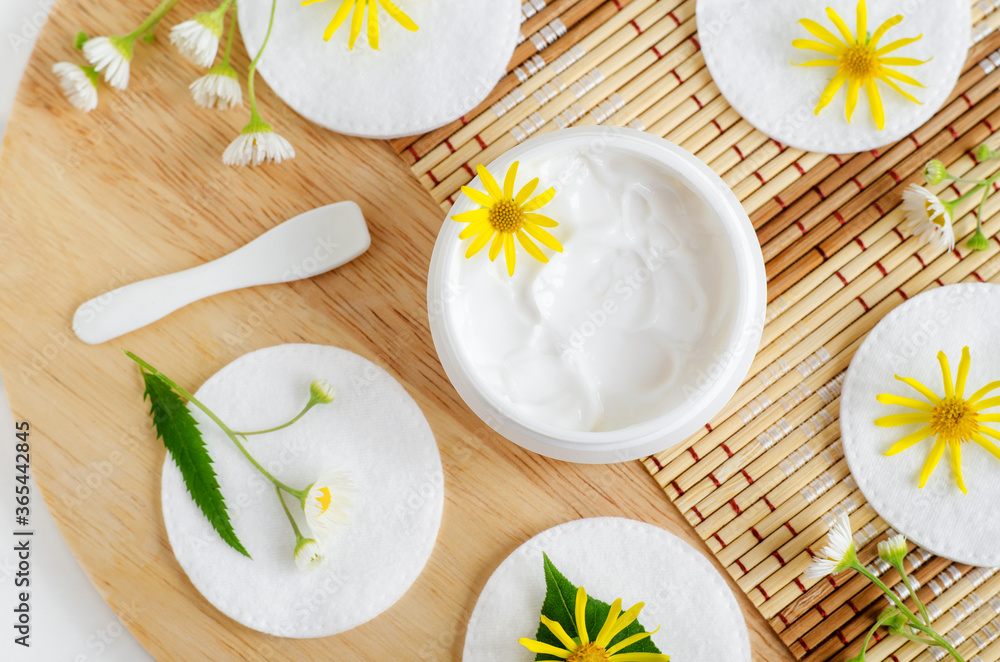 White facial mask (face cream, hair mask, body butter, facial cleanser) in the small white jar, cotton pads and wild flowers. Natural skin and hair treatment concept. Top view, copy space. White facial mask (face cream, hair mask, body butter, facial cleanser) in the small white jar, cotton pads and wild flowers. Natural skin and hair treatment concept. Top view, copy space.