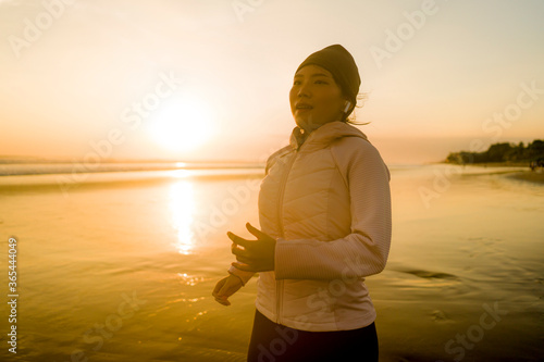 Asian girl running on the beach - young attractive and happy Chinese woman doing jogging workout at beautiful beach enjoying fitness and healthy runner lifestyle