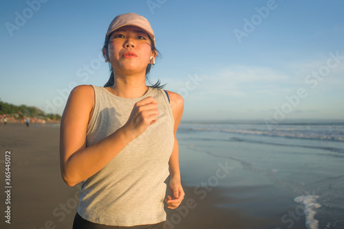 Asian girl running on the beach - young attractive and happy Korean woman doing jogging workout at beautiful beach enjoying fitness and healthy runner lifestyle