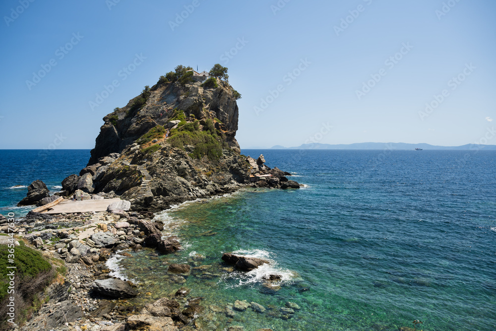 The church of Agios Ioannis on the Mamma Mia Cliff on the island of Skopelos, surrounded by the blue Mediterranean sea seen from the coast.