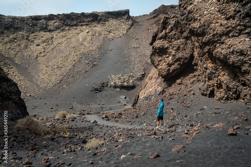 hombre joven con jersey azul, contempla el crater del Volcan El Cuervo desde arriba. Lanzarote. Islas Canarias