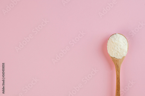  White collagen powder on a wooden spoon on a pink background. Skin care, rejuvenation. Copy space.