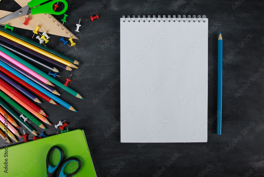 White page of notebook with blue pencil, copy space for text. Green notebook, scissors, pins, ruler on blackboard background. Top view, flat lay. School supplies or office stationery concept White page of notebook with blue pencil, copy space for text. Green notebook, scissors, pins, ruler on blackboard background. Top view, flat lay. School supplies or office stationery concept