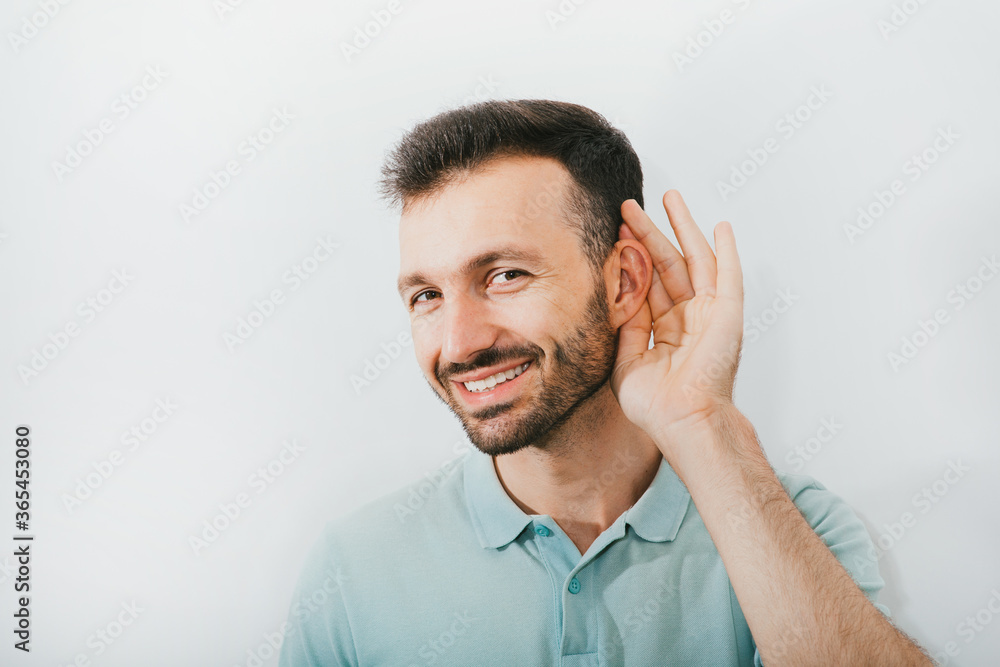Check your hearing. Positive man holds his hand near his ear, on a gray background. Ear health, treatment and diagnosis of hearing Check your hearing. Positive man holds his hand near his ear, on a gray background. Ear health, treatment and diagnosis of hearing