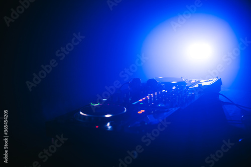 Headphones on DJ mixer console board panel in night club with blue light and smoke.