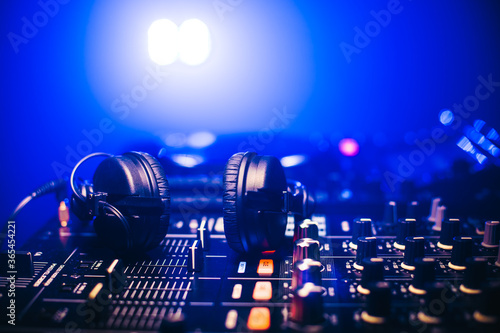 Close up of headphones on Disc jockey mixing board in night club with blue light. © BASILICOSTUDIO STOCK