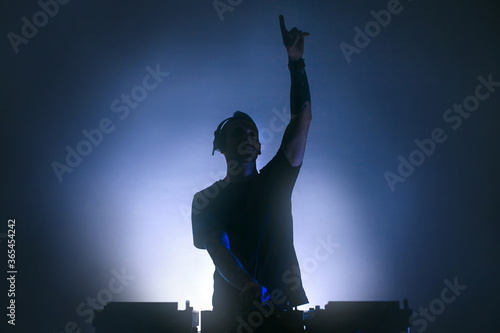 Fotografie Black silhouette of a Male Disc jockey playing music raising an arm up
