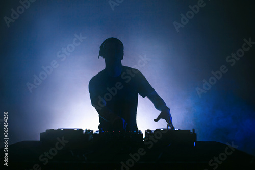 Black silhouette of a Male Disc jockey playing music with a Mixer.