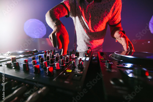 Close up of hands of a male DJ playing the mixer table for techno music in a dark colorful atmosphere.