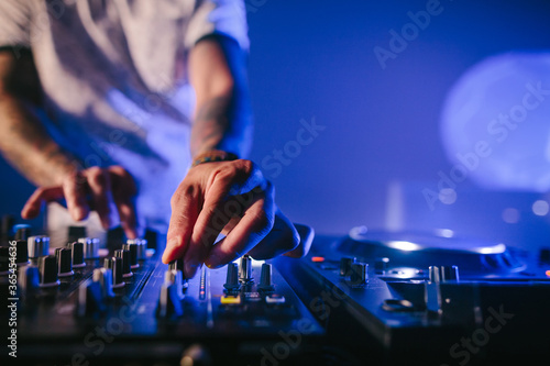 Hands of a male Caucasian DJ playing music on a mixer table in a blue atmosphere. Close up shot.