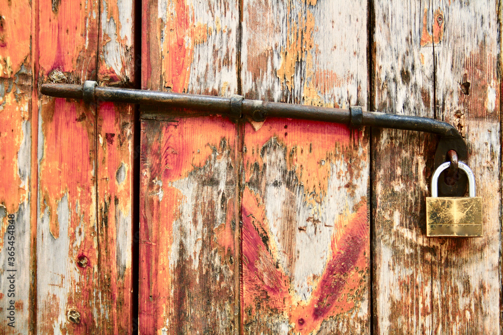 Old rusty padlock on wooden door. Shabby barn gate with a lock and piece of rusty metal. Material: wood with pale orange paint Old rusty padlock on wooden door. Shabby barn gate with a lock and piece of rusty metal. Material: wood with pale orange paint