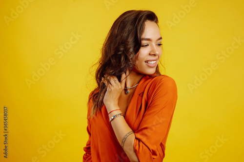 Portrait of young girl posing on yellow background. Pretty woman wears a carrot blouse and jeans. Fashion and lifestyle concept.