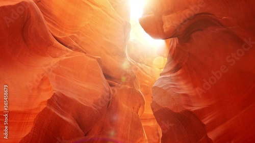 Dust floating around orange sandstone rocks in Antelope Canyon, Arizona, USA. Sun shining through with flare. Steadicam shot, 4K