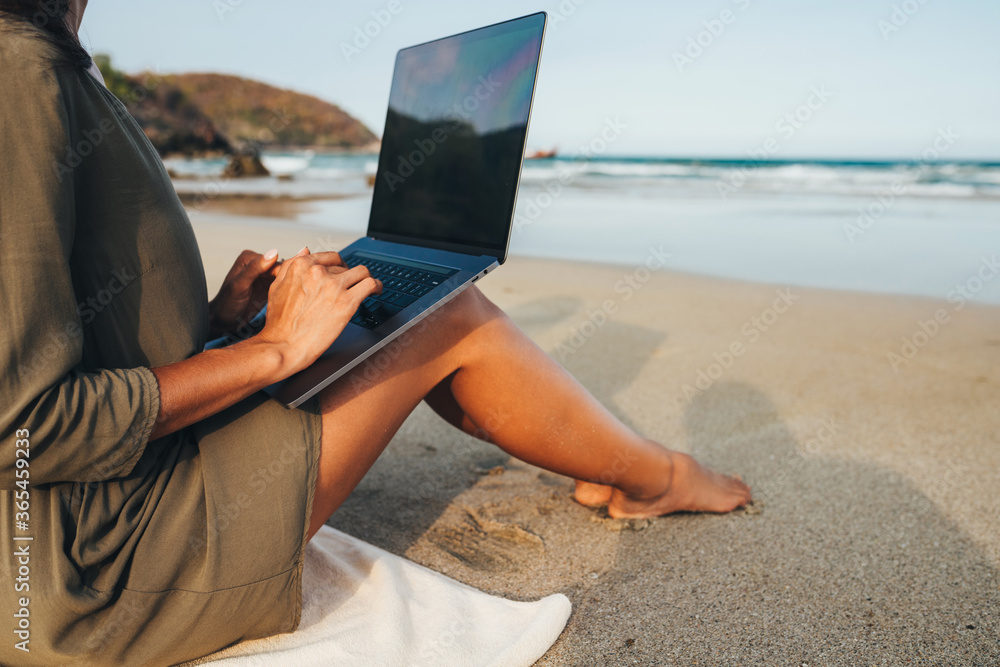 Young girl freelancer works sitting on a rocky beach by the sea at sunset, working in a non-office. The concept of remote work