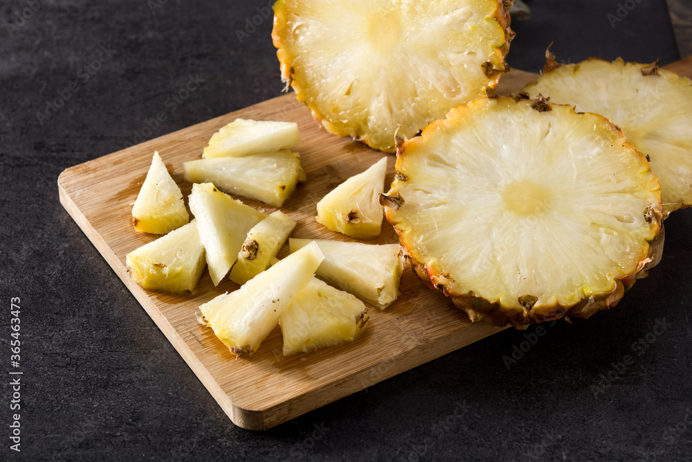 Fresh pineapple slices on cutting board and black stone background Fresh pineapple slices on cutting board and black stone background