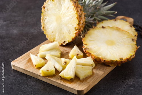 Fresh pineapple slices on cutting board and black stone background 