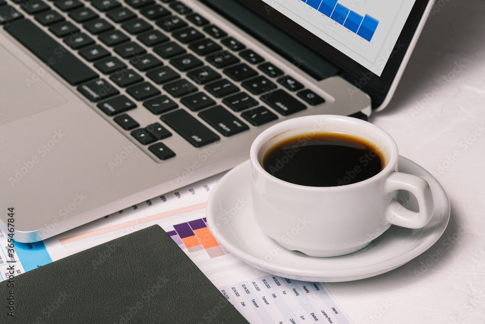 Laptop, a cup of coffee, and analytical charts. Desktop of a businessman. The concept of finance and investment Laptop, a cup of coffee, and analytical charts. Desktop of a businessman. The concept of finance and investment