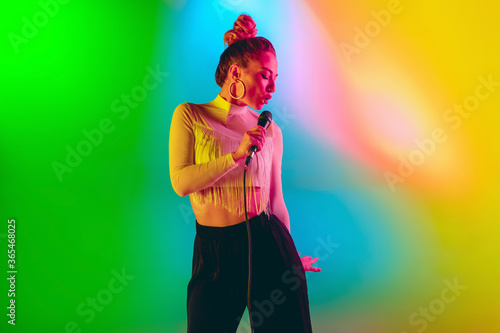 Bright mood. Young female caucasian inspired and expressive musician, singer performing on multicolored background in neon. Concept of music, hobby, festival, art. Joyful artist, colorful portrait.
