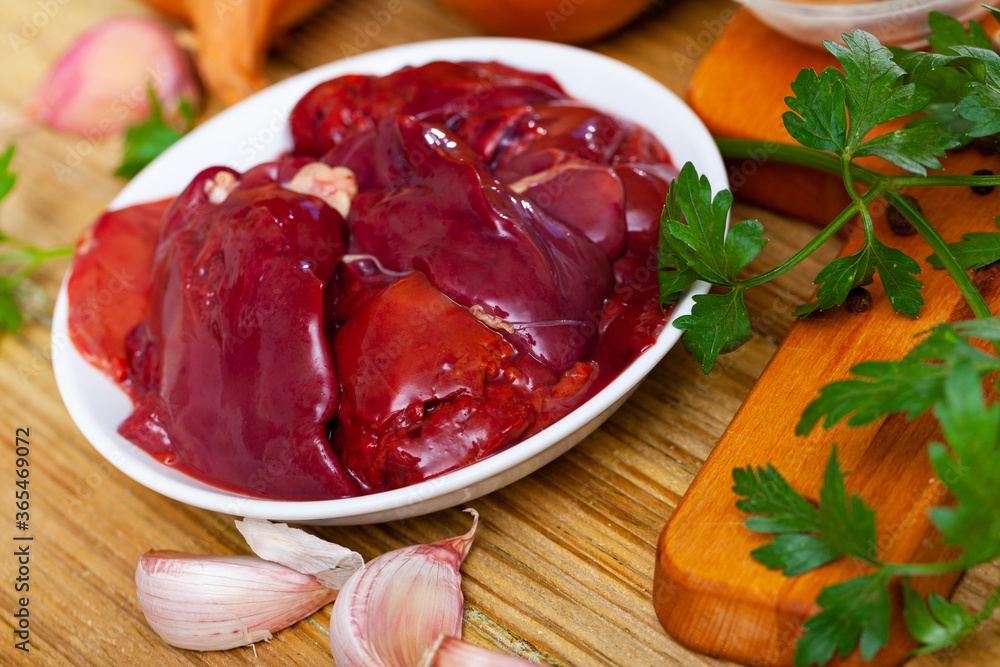 Fresh chicken liver on wooden background with parsley, garlic and onion