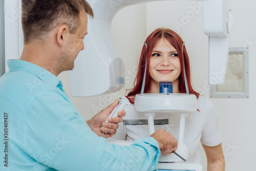 A girl patient makes a panoramic X-ray of the oral cavity on an orthopantomographic apparatus, and the dentist takes a picture photo