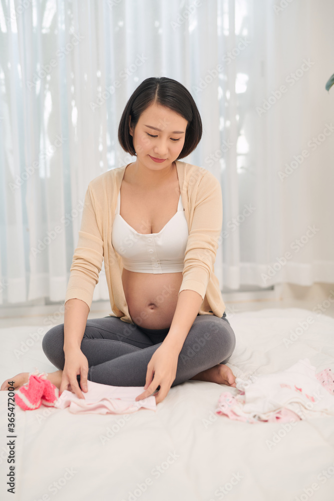 Happy future mother holding in hands cute bodywear for newborn. Concept of parenthood, preparing during pregnancy Happy future mother holding in hands cute bodywear for newborn. Concept of parenthood, preparing during pregnancy