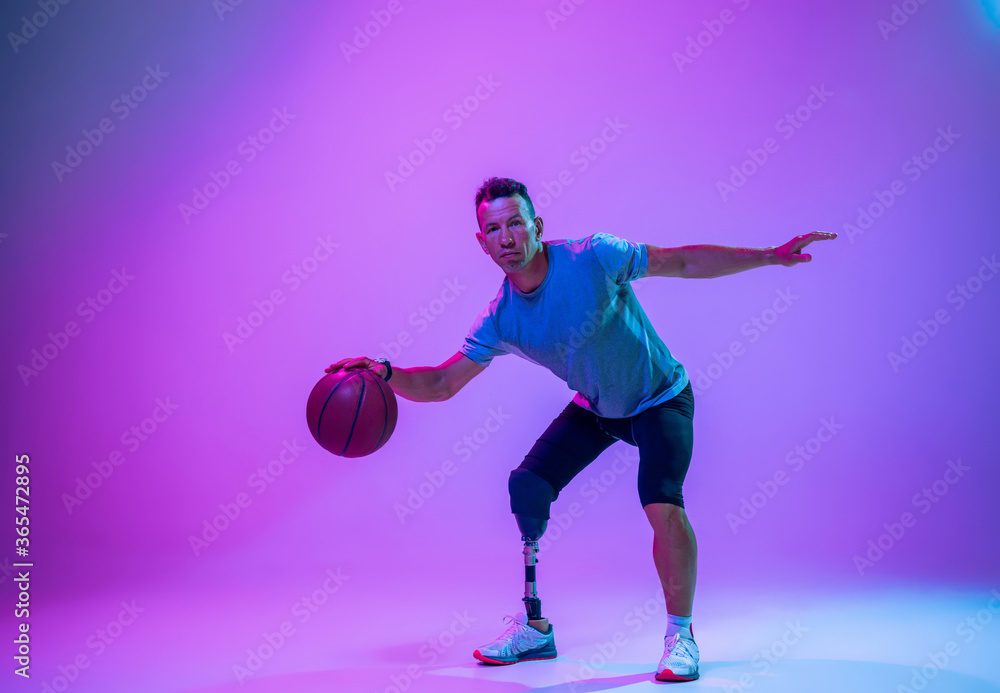 Athlete with disabilities or amputee on gradient studio background in neon. Professional male basketball player with leg prosthesis training in studio. Disabled sport and healthy lifestyle concept. Athlete with disabilities or amputee on gradient studio background in neon. Professional male basketball player with leg prosthesis training in studio. Disabled sport and healthy lifestyle concept.