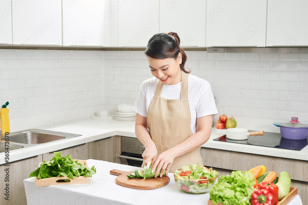 Young smiling housewife preparing healthy meal with vegetables in bright modern kitchen Young smiling housewife preparing healthy meal with vegetables in bright modern kitchen