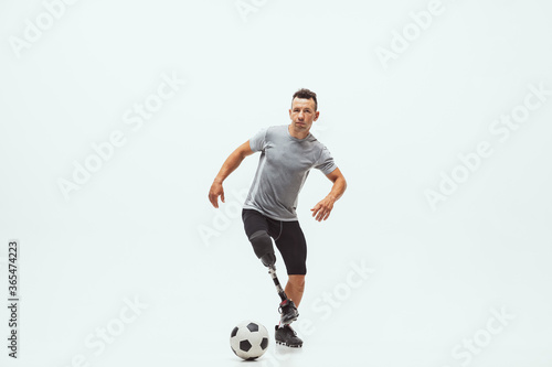 Fototapeta Naklejka Na Ścianę i Meble -  Athlete with disabilities or amputee on white studio background. Professional male football player with leg prosthesis training in studio. Disabled sport and healthy lifestyle concept. Achievements.