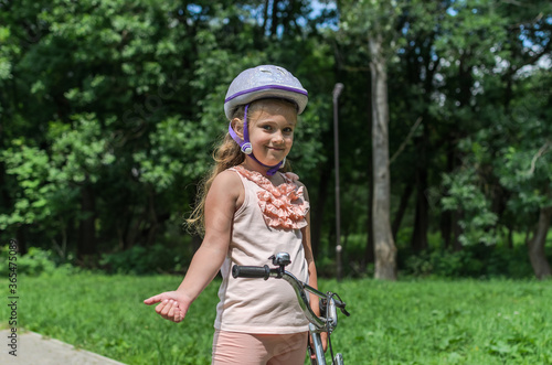 Little charming girl in a bicycle helmet rides a bicycle in the park 