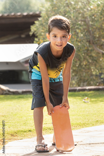 Un bambino biondo con tratti brasiliani si diverte a giocare con lo Skate sulla stradina di un parco photo
