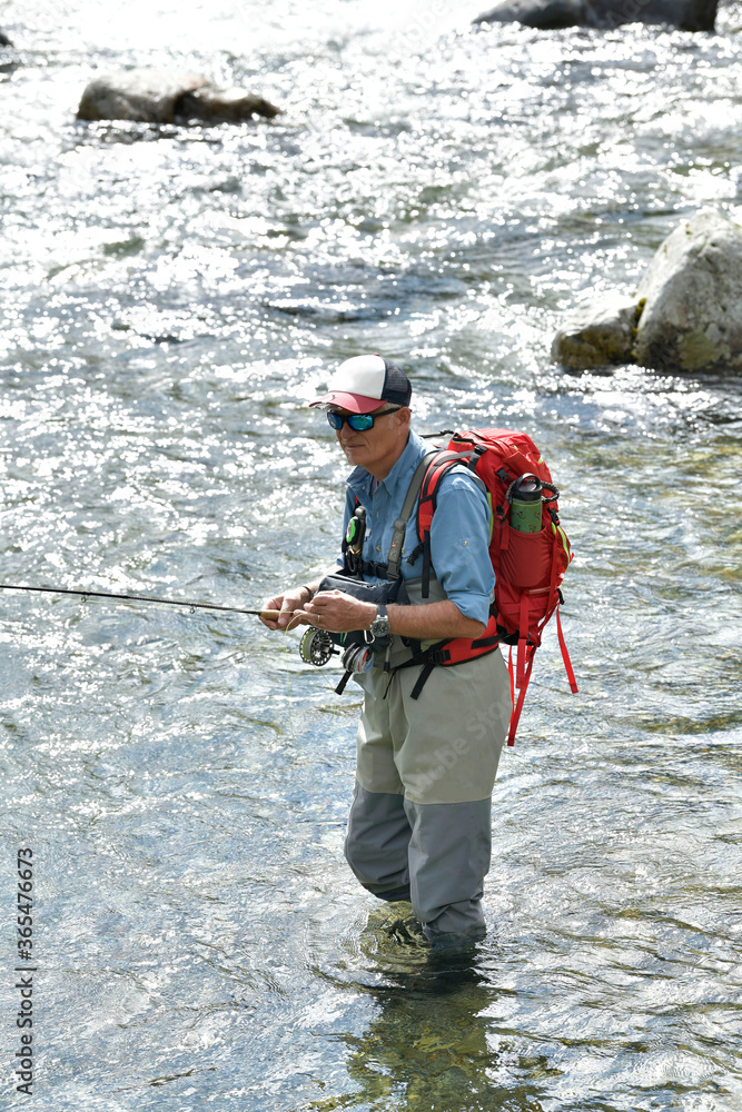 fly fisherman trout fishing with a hiking backpack and a blue shirt in the high mountains in summer fly fisherman trout fishing with a hiking backpack and a blue shirt in the high mountains in summer