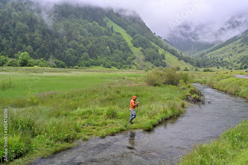 fly fisherman with an orange jacket fishing for trout in the mountains in rainy weather