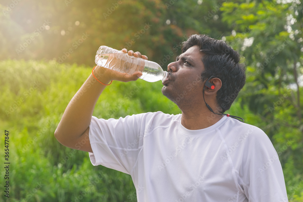 CloseUp Man drinking water after running. Portrait Of handsome athletic male in white sportswear, drink water from bottle on green Background. CloseUp Man drinking water after running. Portrait Of handsome athletic male in white sportswear, drink water from bottle on green Background.