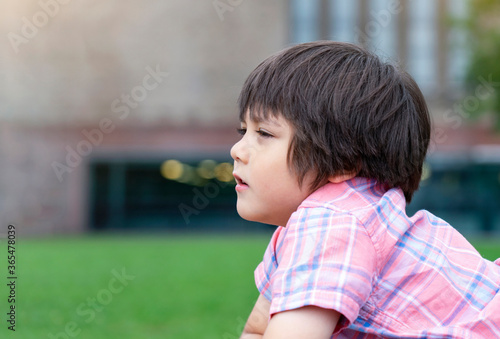 Side view portrait of little boy looking out with thinking face, Head shot Kid lying down on grass in the park, Child relaxing outside in weekend.