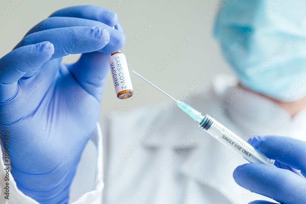 Doctor holds a syringe with a needle in one hand and a container with the COVID-19 vaccine in the other. Doctor holds a syringe with a needle in one hand and a container with the COVID-19 vaccine in the other.