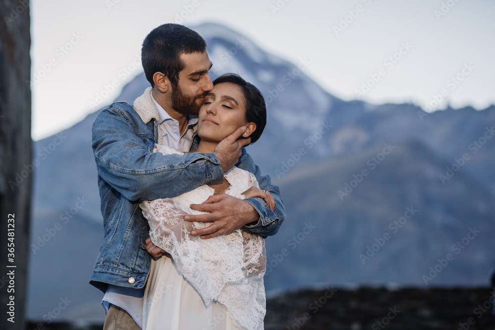 Young Georgian couple posing in the mountains. Boho wedding in Georgia. Evening setting sun. Blue jeans jacket Young Georgian couple posing in the mountains. Boho wedding in Georgia. Evening setting sun. Blue jeans jacket