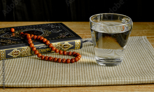 Glass of clear water, rosary and book of Quran. First drink, Muslim fast Eid al, Uraza photo