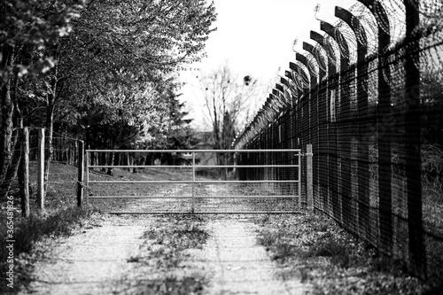 black and white metal gate with a high fence on a forest road