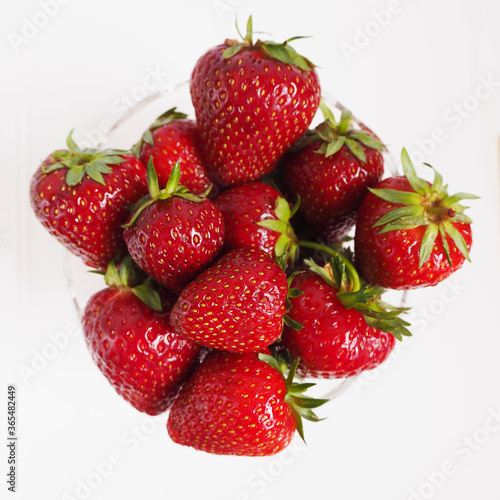 red ripe strawberries in a transparent glass plate top view on a light gray background
